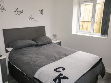 A bedroom with a double bed with dark gray bedding a window and wall decals with words at Sunnydene in Paignton