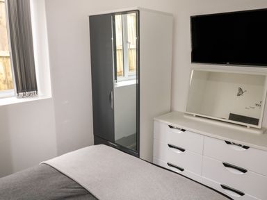 A bedroom with a bed, a wardrobe with mirrored doors, a dresser with a mirror, and a wall-mounted TV at Sunnydene in Paignton
