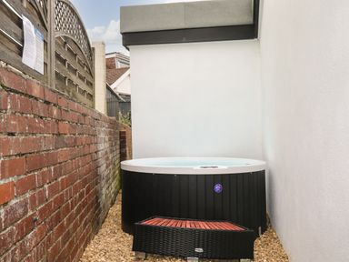 An outdoor hot tub with steps on a gravel surface between a brick wall and a white wall at Sunnydene in Paignton