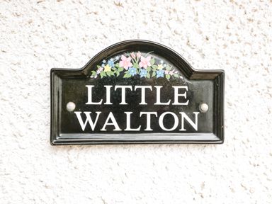 A black sign with flowers reading Little Walton on a white textured wall at Little Walton in Burnham-On-Sea