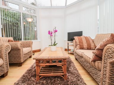 A conservatory with wicker sofas a wooden coffee table with a plant and a television on a stand at Little Walton in Burnham-On-Sea
