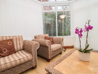 A seating area with two woven armchairs with striped cushions and a potted orchid on a table at Little Walton in Burnham-On-Sea