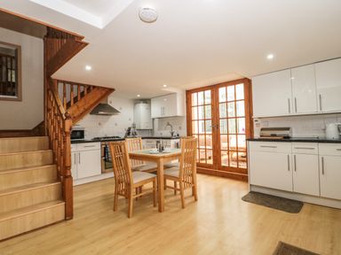 A kitchen with wooden stairs a dining table and chairs white cabinets and glass doors at Little Walton in Burnham-On-Sea