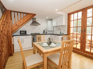 A kitchen with white cabinets a dining table with four chairs wooden staircase and glass doors leading to a seating area at Little Walton in Burnham-On-Sea