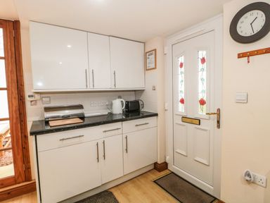 A kitchen corner with white cabinets countertop appliances a door with floral stained glass and a wall clock at Little Walton in Burnham-On-Sea
