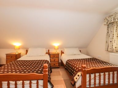 A bedroom with two single wooden beds with brown polka dot blankets and bedside tables with lamps at Little Walton in Burnham-On-Sea