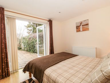 A bedroom with a bed covered in checkered bedding and a brown blanket next to open glass doors leading to a patio at Little Walton in Burnham-On-Sea