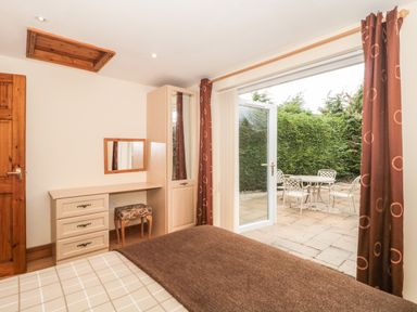 A bedroom with a bed, dressing table with drawers, stool, mirror, wardrobe and an open door to a patio with a table and chairs at Little Walton in Burnham-On-Sea