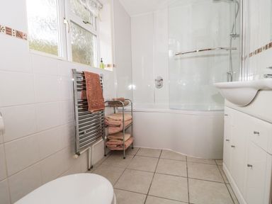 A bathroom with a toilet sink with cabinet tiled floor bathtub with shower and glass screen and towel rack with towels at Little Walton in Burnham-On-Sea