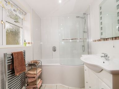 A bathroom with a bathtub shower combo a sink with cabinet a towel rack and a window at Little Walton in Burnham-On-Sea