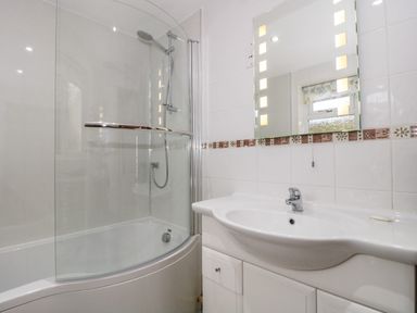 A bathroom with a shower bathtub combination a glass shower screen a sink with a faucet and a lighted mirror above at Little Walton in Burnham-On-Sea