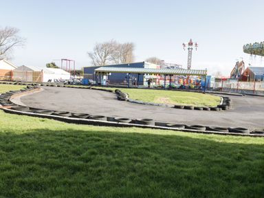An outdoor go-kart track with tires bordering the asphalt and amusement rides in the background at Little Walton in Burnham-On-Sea