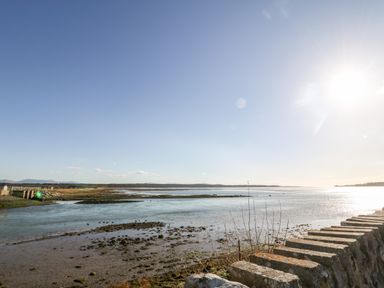 A coastal landscape with water mudflats and a stone wall under a clear sky at Malltraeth Cottage in Malltraeth