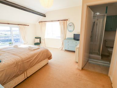 A bedroom with a bed towels a window a chair a dresser with a television and an ensuite bathroom at Malltraeth Cottage in Malltraeth