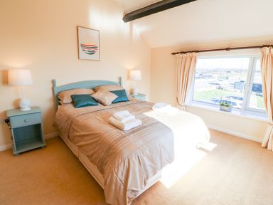 A bedroom with a bed with pillows and folded towels two bedside tables with lamps and a window with curtains at Malltraeth Cottage in Malltraeth