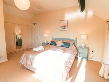 A bedroom with a double bed two bedside tables with lamps a wardrobe with a mirror and a framed picture on the wall at Malltraeth Cottage in Malltraeth