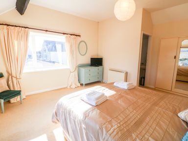 A bedroom with a large bed with folded towels a window with curtains a dresser with a television and a chair at Malltraeth Cottage in Malltraeth