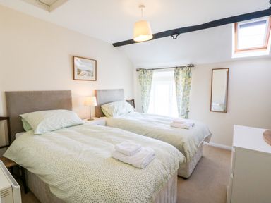 A bedroom with two single beds a nightstand lamp floral curtains a wall mirror and a skylight at Malltraeth Cottage in Malltraeth
