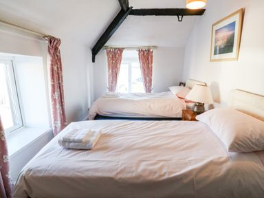 A bedroom with two single beds pink curtains and a bedside table with a lamp at Malltraeth Cottage in Malltraeth