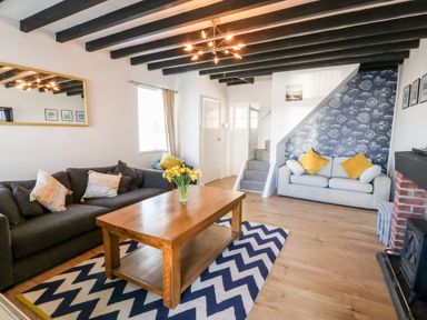A living room with two sofas a wooden table and a patterned rug at Malltraeth Cottage in Malltraeth