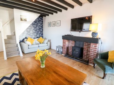A living room with a wooden coffee table and a vase of yellow flowers at Malltraeth Cottage in Malltraeth