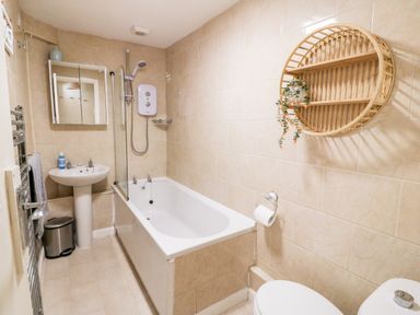 A bathroom with a bathtub shower sink toilet round wall shelf and towel rail at Malltraeth Cottage in Malltraeth