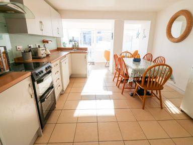 A kitchen with white cabinets wooden countertops a black stove and a dining table with six wooden chairs at Malltraeth Cottage in Malltraeth