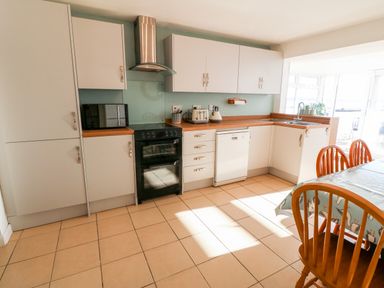 A kitchen with white cabinets black oven white dishwasher wooden dining table and chairs at Malltraeth Cottage in Malltraeth