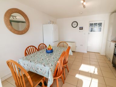 A kitchen with a table covered with a bird patterned tablecloth and six wooden chairs at Malltraeth Cottage in Malltraeth