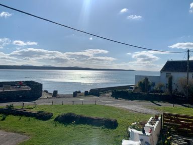 A grassy area with hedges and a white fence beside a road leading to a stone wall and benches by the water at Malltraeth Cottage in Malltraeth