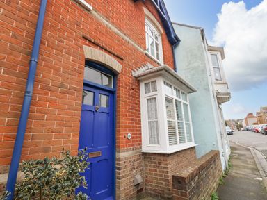 A brick house with a blue door and white bay window on a street at ODYSEA in Weymouth