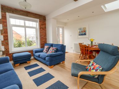 A living room with blue sofas and an armchair a round wooden dining table with chairs and flowers on it at ODYSEA Weymouth