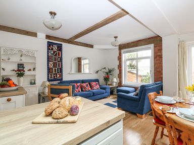A living room with blue sofas a wooden dining table and a kitchen counter with bread at ODYSEA in Weymouth