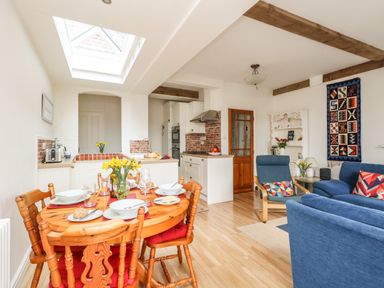 An open plan dining and living area with a wooden dining table set for four and blue upholstered sofas at ODYSEA Weymouth