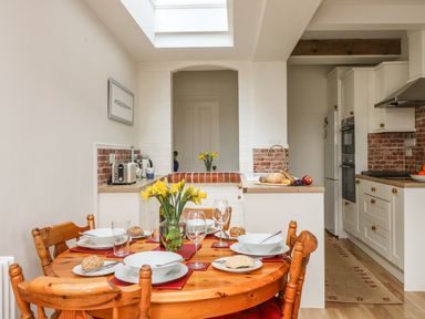 A dining table set with plates and glasses in a kitchen with white cabinets and wooden chairs at ODYSEA in Weymouth
