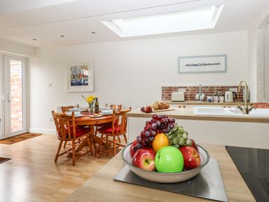 A kitchen and dining area with a fruit bowl on a counter wooden dining table set with plates and wine glasses at ODYSEA in Weymouth