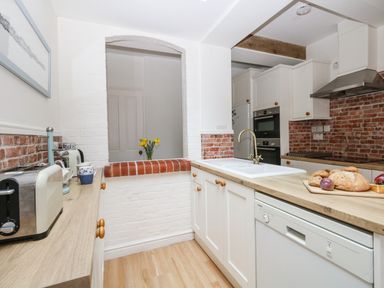 A kitchen with white cabinets a wooden countertop a sink a toaster and a cutting board with bread and onions at ODYSEA in Weymouth
