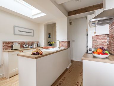 A kitchen with white cabinets wooden countertops a sink an island with bread and fruit and brick backsplash at ODYSEA Weymouth