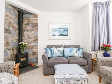 A living room with a grey sofa and blue cushions a wood burning stove with flowers and patterned armchairs at ODYSEA Weymouth