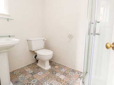 A bathroom with a toilet sink glass shower enclosure and patterned tile floor at ODYSEA in Weymouth