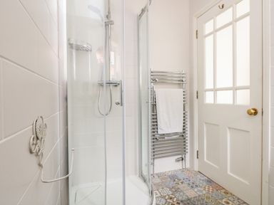 A bathroom with a glass shower enclosure a white towel on a wall-mounted chrome radiator and a white door with glass panels at ODYSEA in Weymouth