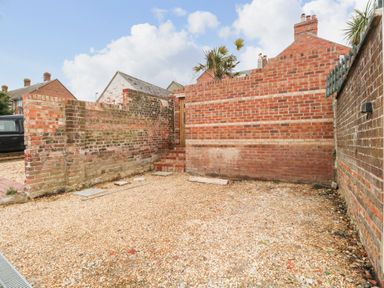 An outdoor area with gravel ground and brick walls including steps leading to a wooden gate at ODYSEA in Weymouth