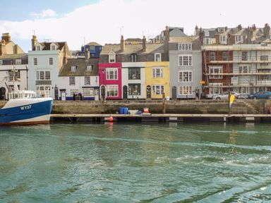 A row of colorful houses along a waterfront with a blue boat docked at the pier at ODYSEA Weymouth