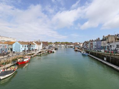 A harbor with boats docked along both sides and buildings lining the waterfront at ODYSEA Weymouth