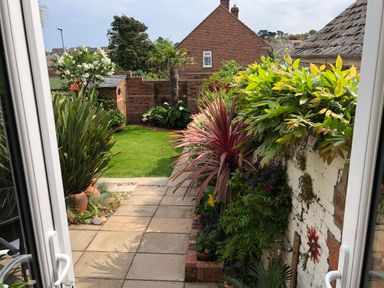 A garden with plants and flowers along a stone path and a lawn visible through an open door at ODYSEA in Weymouth