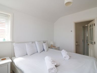 A bedroom with a white bed and pillows two rolled towels bedside tables a lamp and an open door to a bathroom at ODYSEA in Weymouth