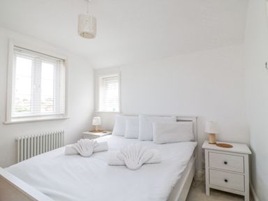 A bedroom with a white bed and folded towels on it two bedside tables with lamps and windows with blinds at ODYSEA Weymouth
