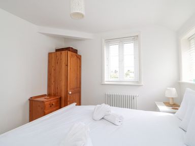 A bedroom with a wooden wardrobe and chest of drawers near a window with blinds and a bedside table with a lamp at ODYSEA Weymouth