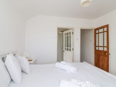 A bedroom with a white bed and pillows towels on the bed a nightstand with a lamp white and wooden doors at ODYSEA Weymouth