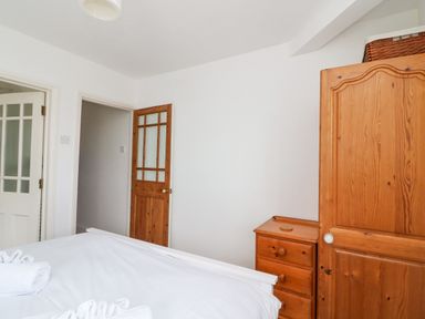 A bedroom with a wooden wardrobe and chest of drawers beside a bed with white bedding at ODYSEA in Weymouth